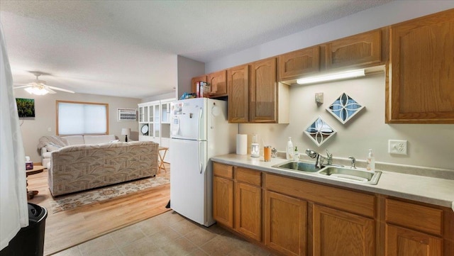 kitchen with light countertops, brown cabinetry, freestanding refrigerator, a sink, and a textured ceiling