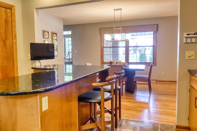 kitchen with dark stone counters, light hardwood / wood-style floors, pendant lighting, and a kitchen breakfast bar