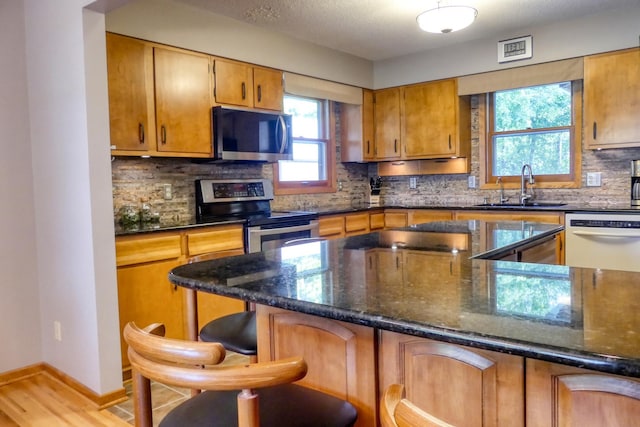 kitchen featuring dark stone countertops, appliances with stainless steel finishes, light hardwood / wood-style floors, decorative backsplash, and sink