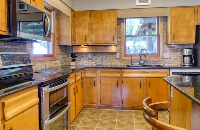 kitchen with appliances with stainless steel finishes, dark stone countertops, a wealth of natural light, and sink