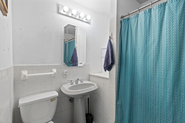 bathroom with tile walls, toilet, wainscoting, a sink, and a shower with curtain