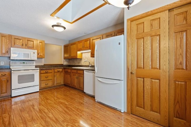 kitchen with sink, white appliances, a skylight, and light hardwood / wood-style flooring