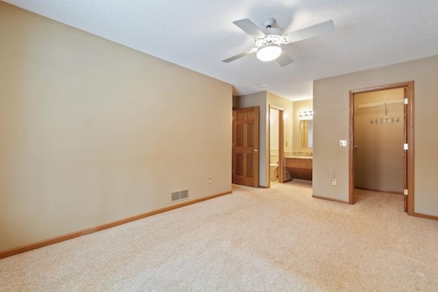 unfurnished bedroom with light carpet, ceiling fan, a closet, a walk in closet, and ensuite bath