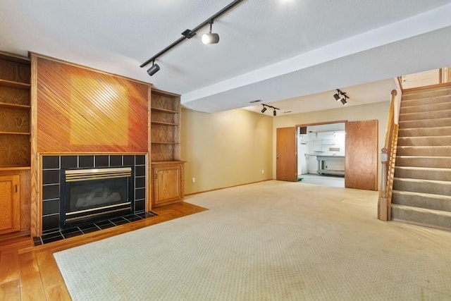 unfurnished living room with track lighting, a tile fireplace, and carpet floors