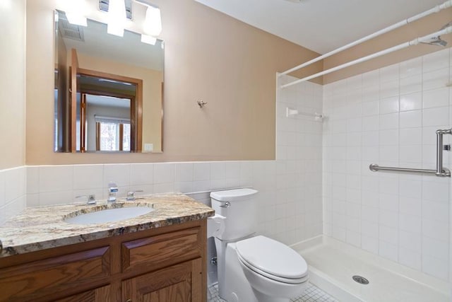 bathroom with vanity, tile patterned flooring, tile walls, toilet, and tiled shower