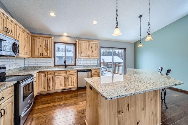 kitchen with decorative light fixtures, a center island with sink, sink, appliances with stainless steel finishes, and a kitchen breakfast bar