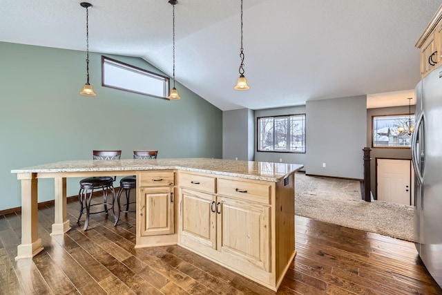 kitchen with lofted ceiling, a center island, a kitchen bar, light brown cabinetry, and stainless steel fridge