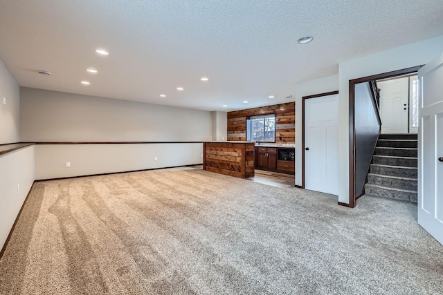 unfurnished living room with a textured ceiling, light colored carpet, and wood walls