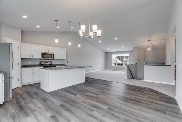 kitchen with appliances with stainless steel finishes, white cabinets, decorative light fixtures, and a center island with sink