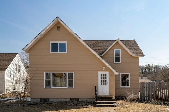 rear view of house with entry steps, a shingled roof, and fence