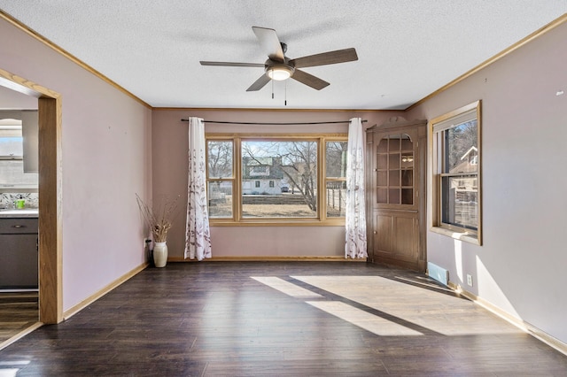 empty room with ornamental molding, a ceiling fan, a textured ceiling, wood finished floors, and baseboards