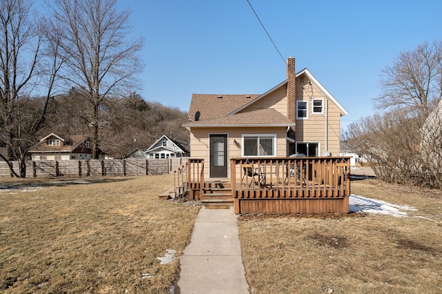 rear view of house featuring fence, roof with shingles, a chimney, a deck, and a lawn