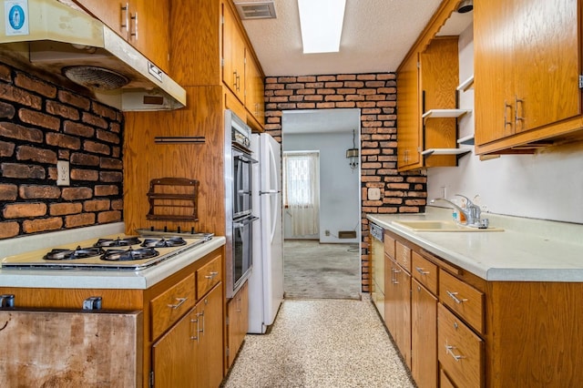 kitchen featuring brick wall, a textured ceiling, double oven, white gas cooktop, and sink