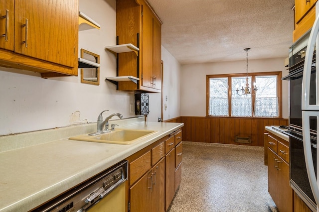 kitchen with a textured ceiling, dishwasher, sink, hanging light fixtures, and wood walls