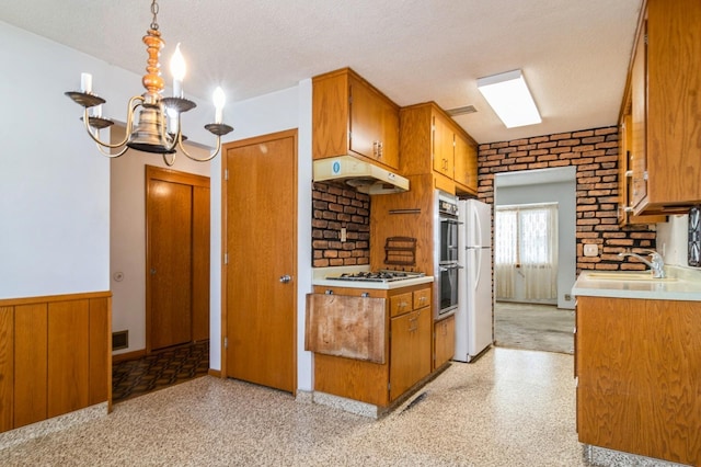 kitchen with wood walls, gas cooktop, decorative light fixtures, a textured ceiling, and sink