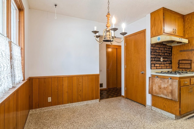 kitchen featuring a textured ceiling, an inviting chandelier, hanging light fixtures, wood walls, and stainless steel gas stovetop