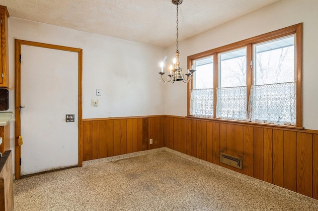 carpeted spare room with an inviting chandelier, wooden walls, and a textured ceiling