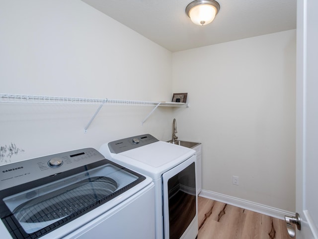 laundry area featuring sink, washer and clothes dryer, and light hardwood / wood-style flooring