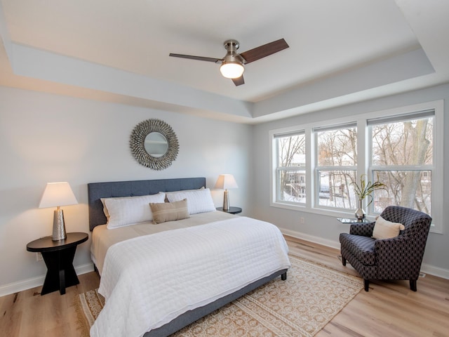 bedroom featuring ceiling fan, light hardwood / wood-style flooring, and a tray ceiling