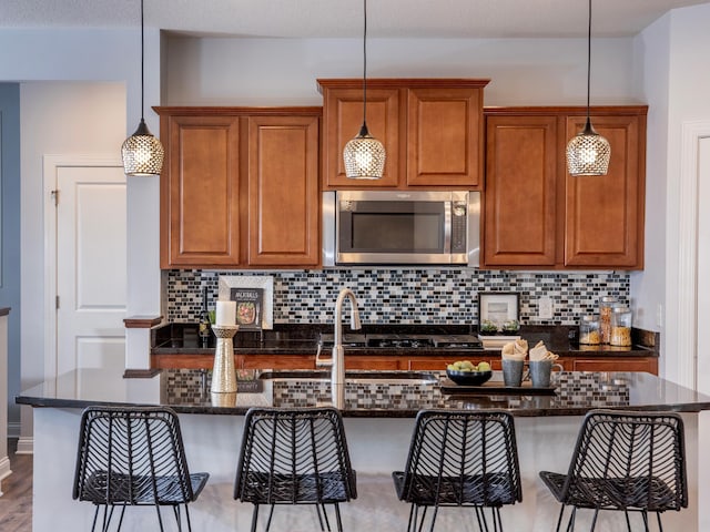 kitchen with a kitchen bar, hanging light fixtures, tasteful backsplash, and an island with sink