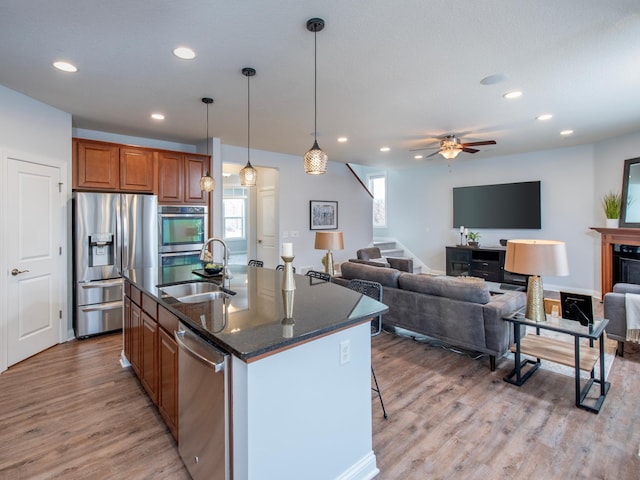 kitchen featuring an island with sink, ceiling fan, stainless steel appliances, wood-type flooring, and sink