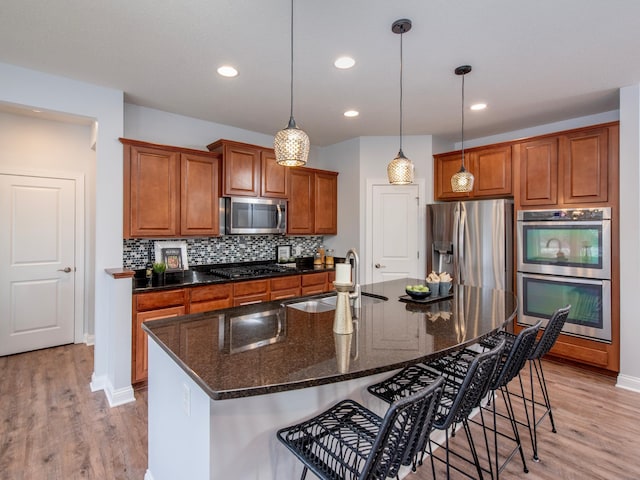 kitchen with a breakfast bar area, stainless steel appliances, a kitchen island with sink, pendant lighting, and sink