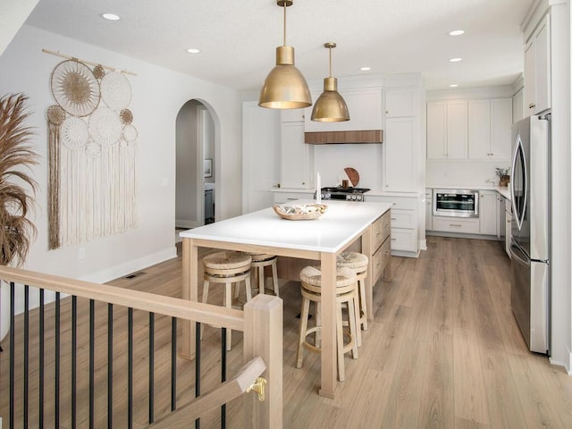 kitchen with light countertops, light wood-style flooring, freestanding refrigerator, and white cabinets