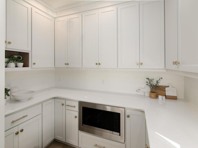 kitchen with white cabinets, open shelves, stainless steel microwave, and light countertops