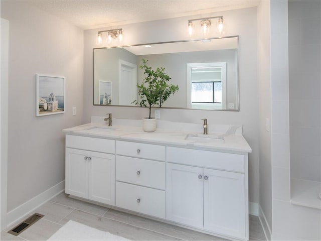 bathroom with a textured ceiling, double vanity, a sink, and visible vents