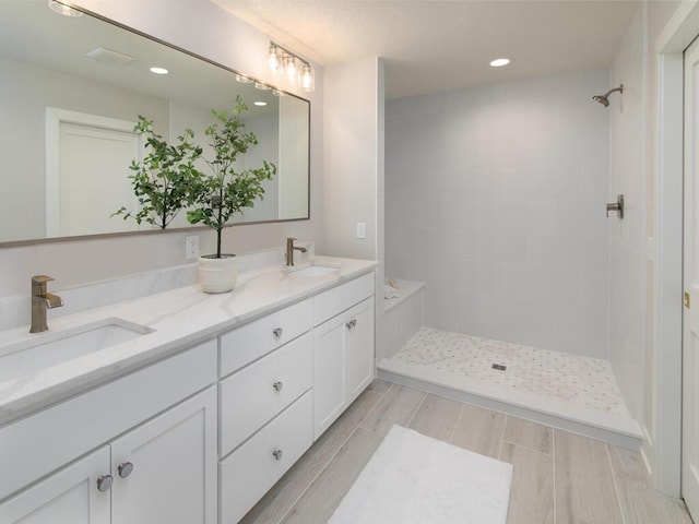 bathroom featuring double vanity, a tile shower, a sink, and recessed lighting