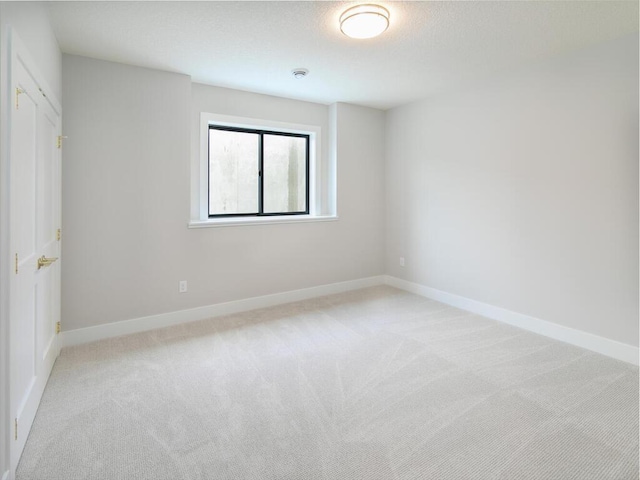 unfurnished room featuring light carpet, a textured ceiling, and baseboards