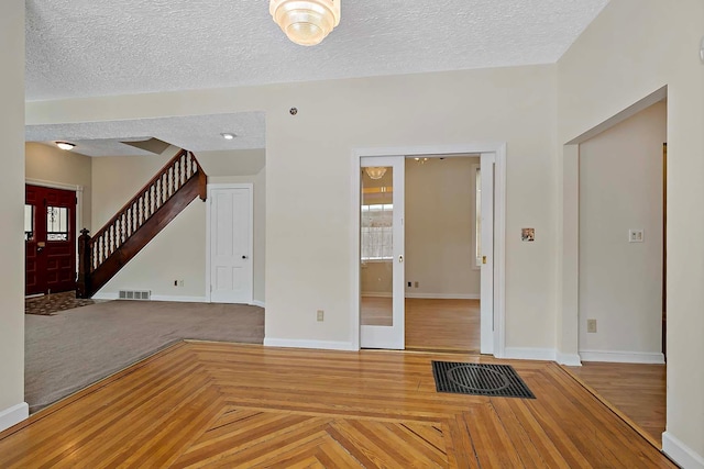 unfurnished living room featuring baseboards, visible vents, stairway, a textured ceiling, and french doors