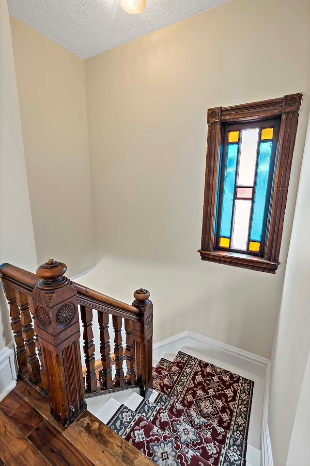 staircase featuring a textured ceiling, wood finished floors, and baseboards