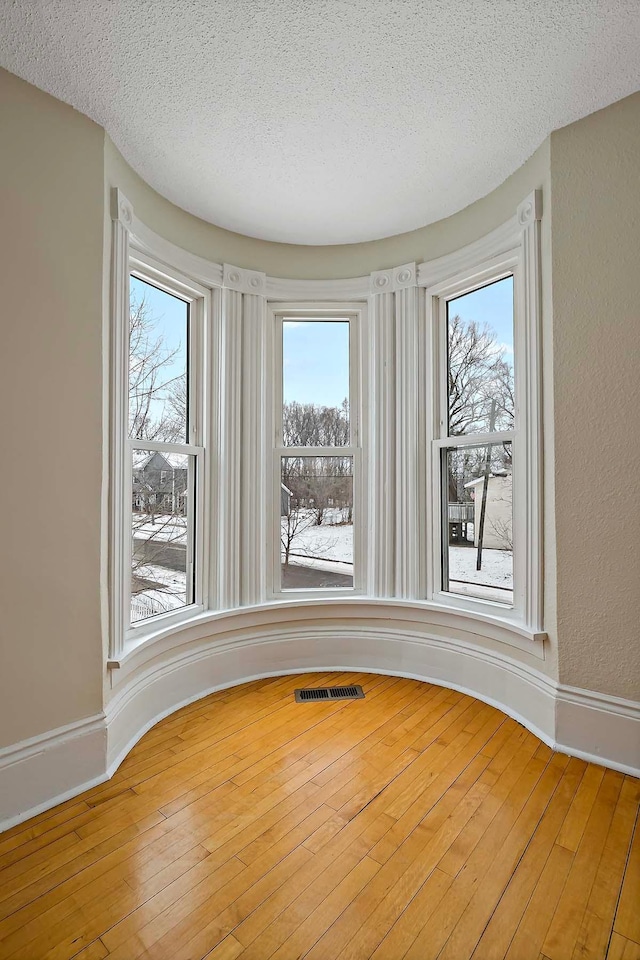 spare room with a textured ceiling, a wealth of natural light, wood finished floors, and visible vents