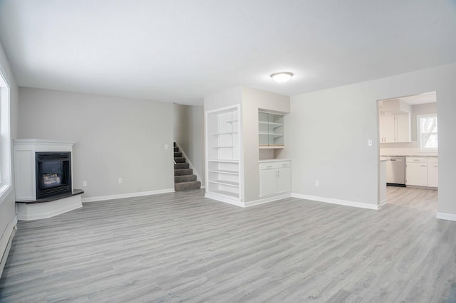 unfurnished living room with built in shelves, a baseboard heating unit, and light hardwood / wood-style flooring