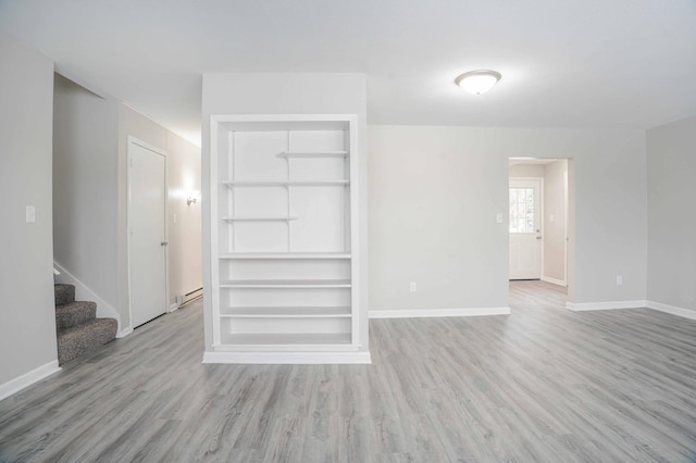 unfurnished living room featuring a baseboard heating unit, light wood-type flooring, and built in shelves