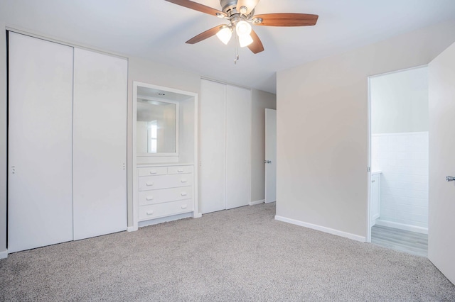 unfurnished bedroom featuring ensuite bathroom, two closets, light colored carpet, and ceiling fan