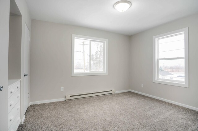 unfurnished room featuring baseboard heating, carpet flooring, and a wealth of natural light