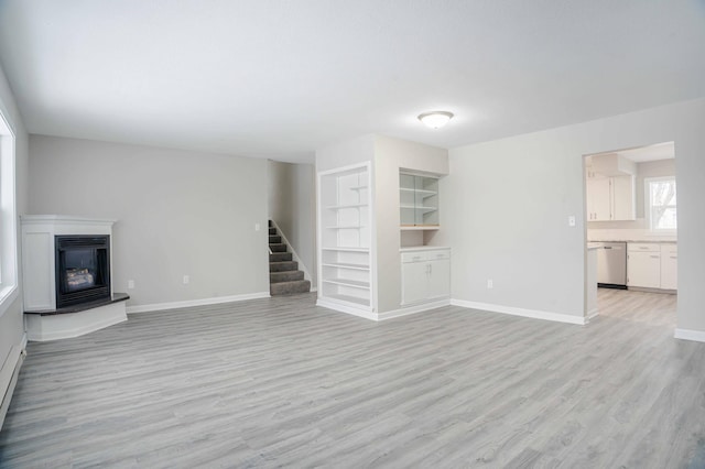 53 Eastview Dr, Hancock, MN 56244 - unfurnished living room with built in shelves, light wood-style floors, stairway, baseboards, and a glass covered fireplace