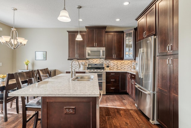 kitchen with a breakfast bar area, appliances with stainless steel finishes, light stone counters, a center island with sink, and decorative light fixtures