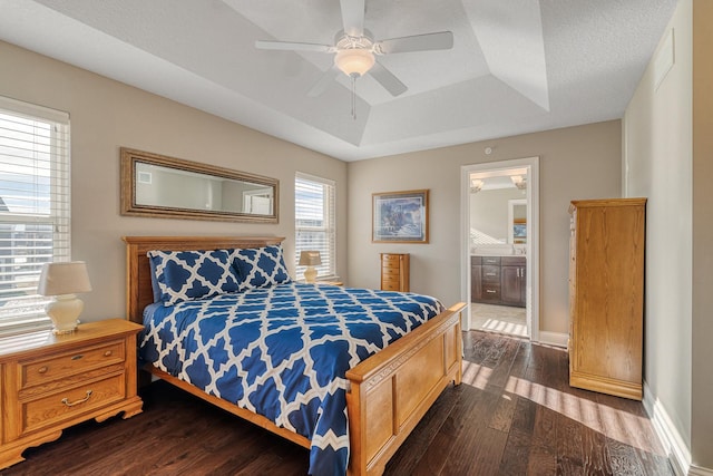 bedroom featuring dark wood-type flooring, ceiling fan, ensuite bathroom, and a tray ceiling