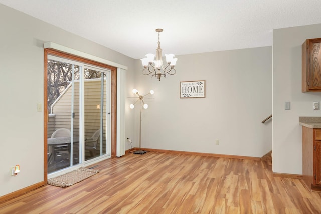 unfurnished dining area featuring an inviting chandelier, a textured ceiling, and light hardwood / wood-style flooring