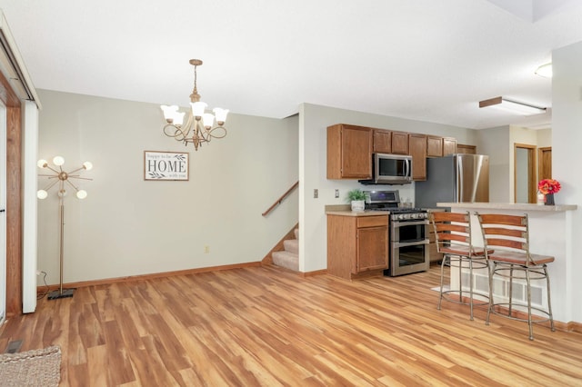 kitchen featuring light hardwood / wood-style flooring, a breakfast bar area, hanging light fixtures, a chandelier, and appliances with stainless steel finishes