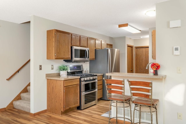 kitchen with stainless steel appliances, kitchen peninsula, a kitchen bar, a textured ceiling, and light hardwood / wood-style flooring