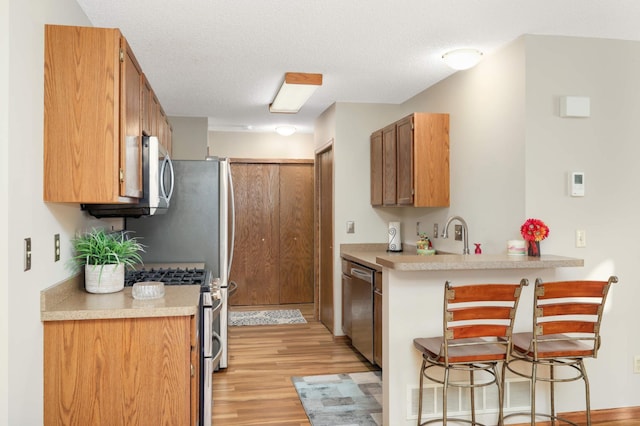 kitchen featuring kitchen peninsula, a textured ceiling, light hardwood / wood-style flooring, and appliances with stainless steel finishes