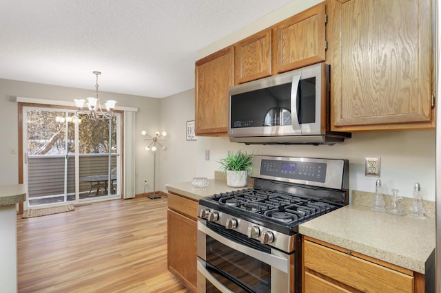 kitchen featuring an inviting chandelier, a textured ceiling, light hardwood / wood-style flooring, hanging light fixtures, and appliances with stainless steel finishes