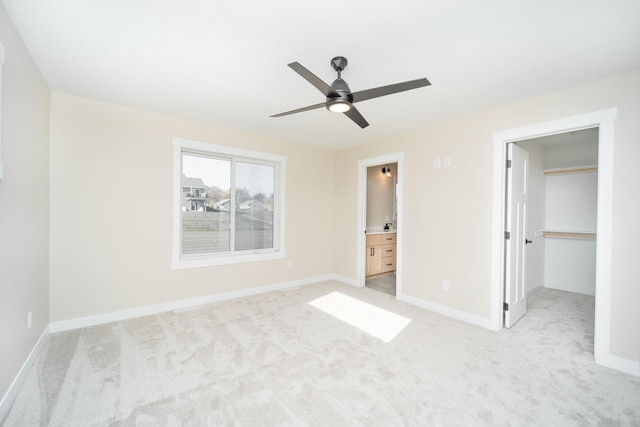 unfurnished bedroom featuring connected bathroom, ceiling fan, a closet, a walk in closet, and light colored carpet