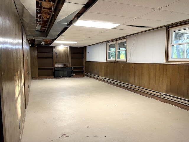 basement featuring a paneled ceiling and wood walls