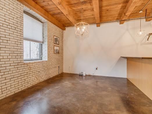 unfurnished room featuring beamed ceiling, brick wall, concrete flooring, and wooden ceiling