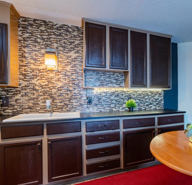 kitchen featuring a textured ceiling, dark brown cabinets, backsplash, and sink